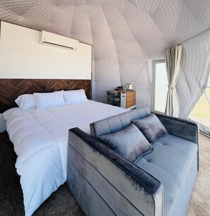 A modern hotel room with a large bed, a sofa, a desk, and a window with curtains.