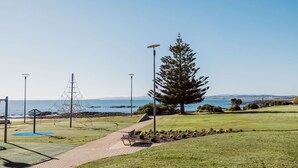 Ein Park mit einem Weg zu einer Bank, einem großen Baum und Blick auf das Meer.
