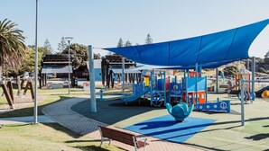 Ein Spielplatz mit einem blauen Sonnensegel, einer Bank und einer Straßenlaterne.