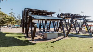 Ein Pavillon mit Metallverkleidung und Holzbalken, umgeben von Picknicktischen und Bänken.