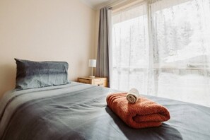 Cama bem arrumada com cobertor cinza e toalha dobrada ao lado.