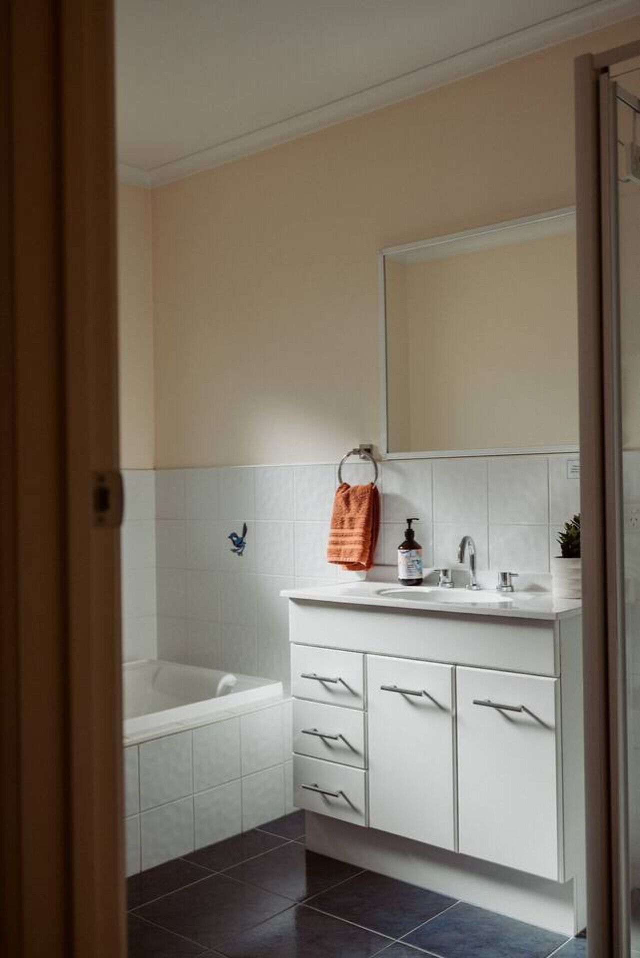 A modern bathroom with a white vanity, a bathtub, and a large mirror.