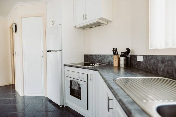A modern kitchen with white cabinets, a built-in oven, a stovetop, and a granite countertop. - The Sanctuary Devonport (Devonport)
