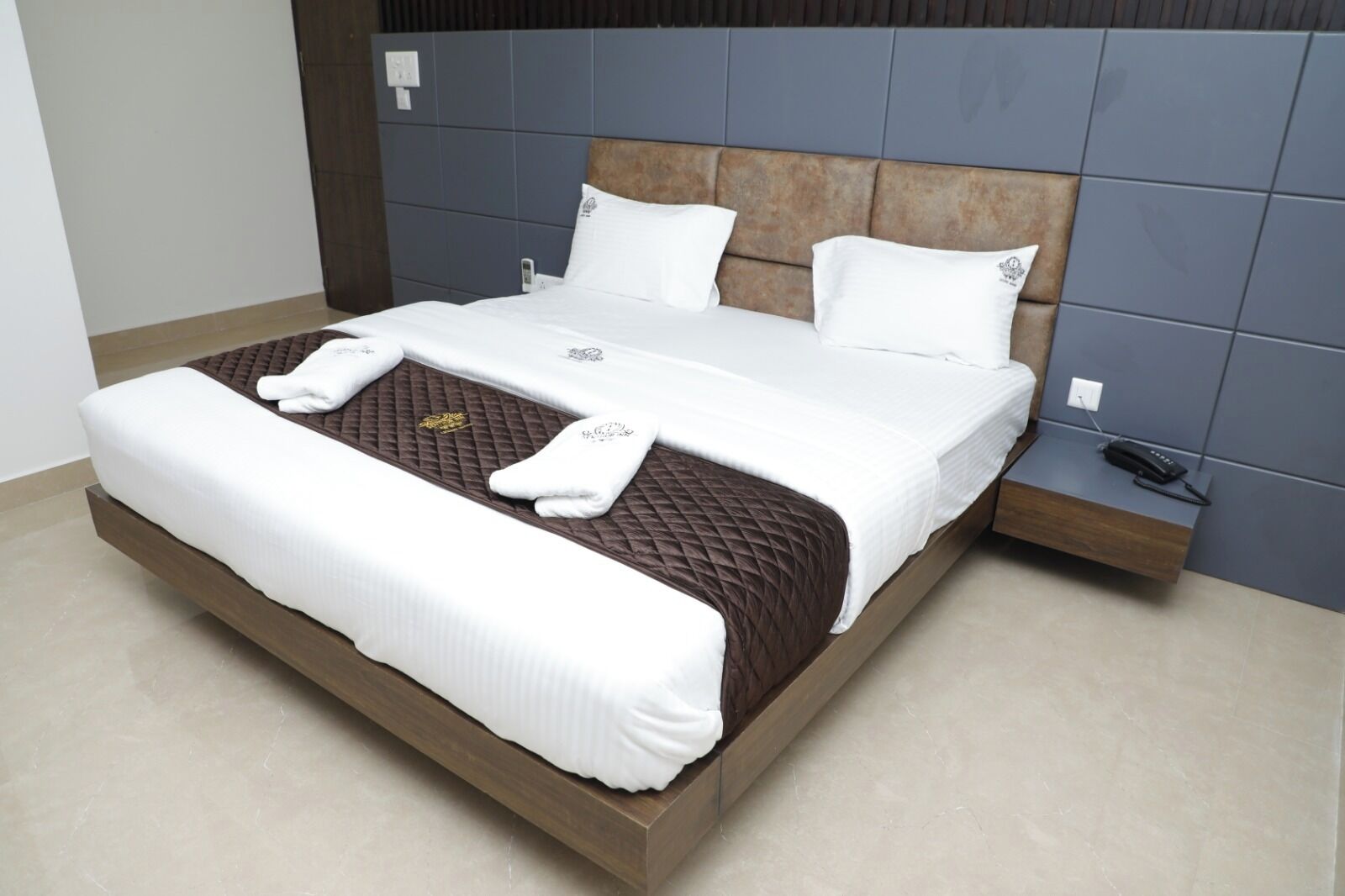 A modern hotel room with a large bed, a wooden headboard, and a bedside table with a phone.