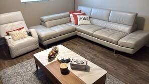 Un saló amb un sofà seccional de cuir beix, una butaca blanca i una taula de centre amb objectes decoratius.