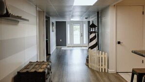 A hallway with a wooden floor, a white door, a black lantern, and a white picket fence. - Pleasant Acres - Pleasant Acres (Greenville)