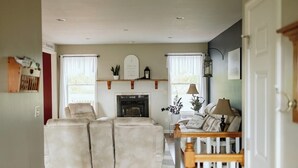 A living room with a fireplace, a sofa set, a wooden bench, and a white railing. - Pleasant Acres - Pleasant Acres (Greenville)