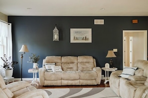 Un salon avec un mur de couleur sombre, un canapé beige, une petite table d’appoint, un lampadaire et un tableau encadré.