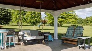 A covered outdoor seating area with a swing, a sofa, and two chairs. - Pleasant Acres - Pleasant Acres (Greenville)