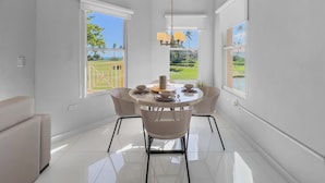 A modern dining area with a round table and wicker chairs, large windows with views of a green landscape, and a ceiling light fixture. - Spacious 3BR apt for 10 Guests | Palmas del Mar (Palmas Del Mar)
