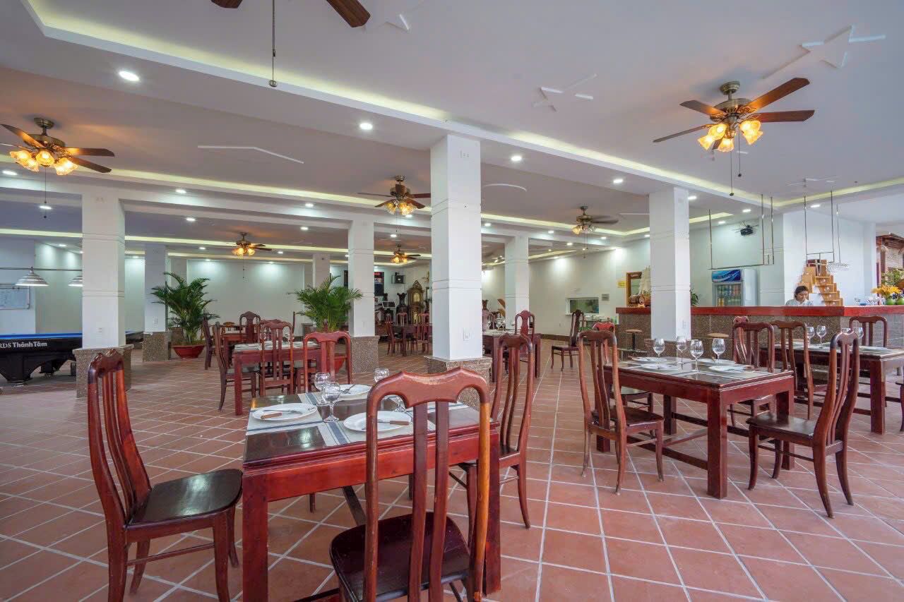 A spacious indoor dining area with multiple tables and chairs, ceiling fans, and potted plants.