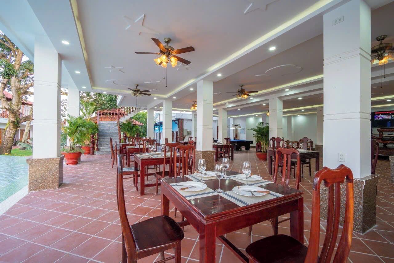 A spacious restaurant with multiple dining areas, ceiling fans, and potted plants.