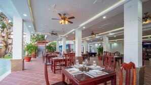 A spacious restaurant with multiple dining areas, ceiling fans, and potted plants. - New Serene (Phu Quoc)