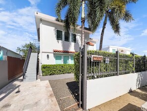 A modern two-story house with a gated entrance, a staircase leading to the main door, and a well-maintained garden with palm trees. - La Casona | Multi Unit House for Groups @ San Juan (San Juan)