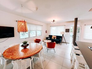 A modern living room with a round wooden table, white chairs, a red sofa, and a television mounted on the wall. - La Casona | Multi Unit House for Groups @ San Juan (San Juan)