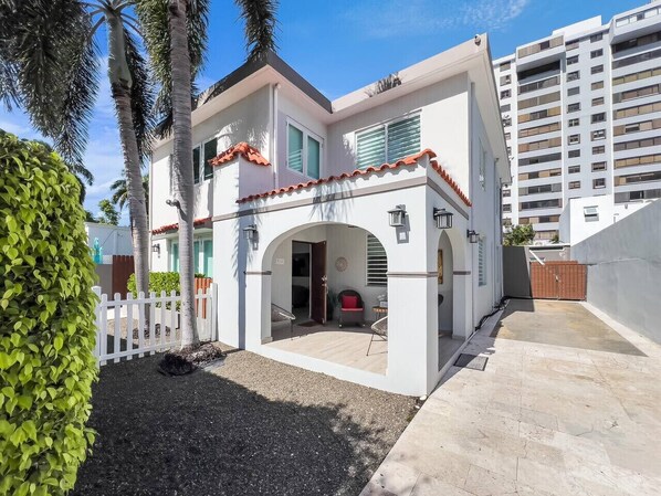 A modern two-story house with a white exterior, a red-tiled roof, and a small patio area with outdoor furniture. - La Casona | Multi Unit House for Groups @ San Juan (San Juan)