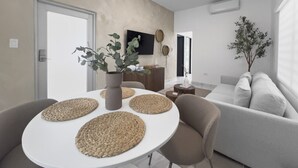 Ein modernes Wohnzimmer mit einem runden weißen Tisch, einem grauen Sofa und einer beige farbenen Wand.
