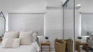 Ein modernes Schlafzimmer mit einem großen Bett, Nachttischen, einem Spiegel und einer Wand-Klimaanlage.