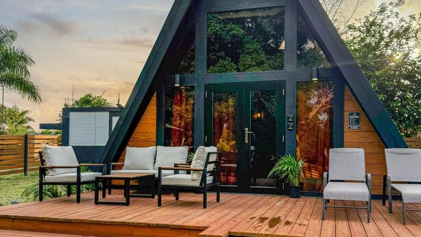 Een modern A-frame gebouw met een zwembad, buitenmeubels en een houten terras.