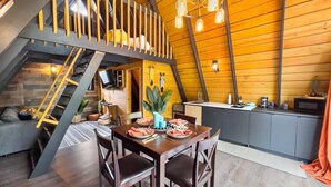 Een eetgedeelte met een houten tafel voor twee personen, een keuken op de achtergrond en een trap naar een hoger gelegen verdieping.