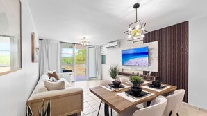 En moderne stue med sofa, spisebord, stole, et fjernsyn og en altan med gardiner.