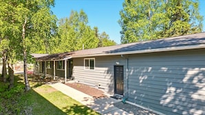 A single-story house with a front porch, a covered entryway, and a small front yard with trees and a lawn.