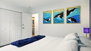A bedroom with a bed, a blue throw blanket, and three wall-mounted paintings of orcas.