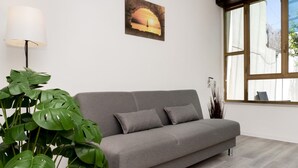 A grey sofa with two cushions, a potted plant, a lamp, and a painting on the wall.