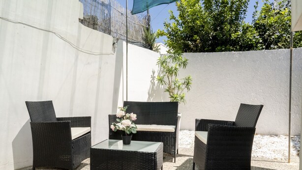 An outdoor patio with wicker furniture, a glass table, and a potted plant.