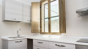 Una cocina moderna con armarios blancos, horno empotrado y ventana con marco dorado.