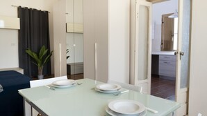 Comedor con una mesa de vidrio dispuesta para cuatro personas, un sofá azul oscuro y una planta en maceta.