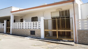 Una casa de dos pisos con balcón, entrada protegida por un muro y chimenea.