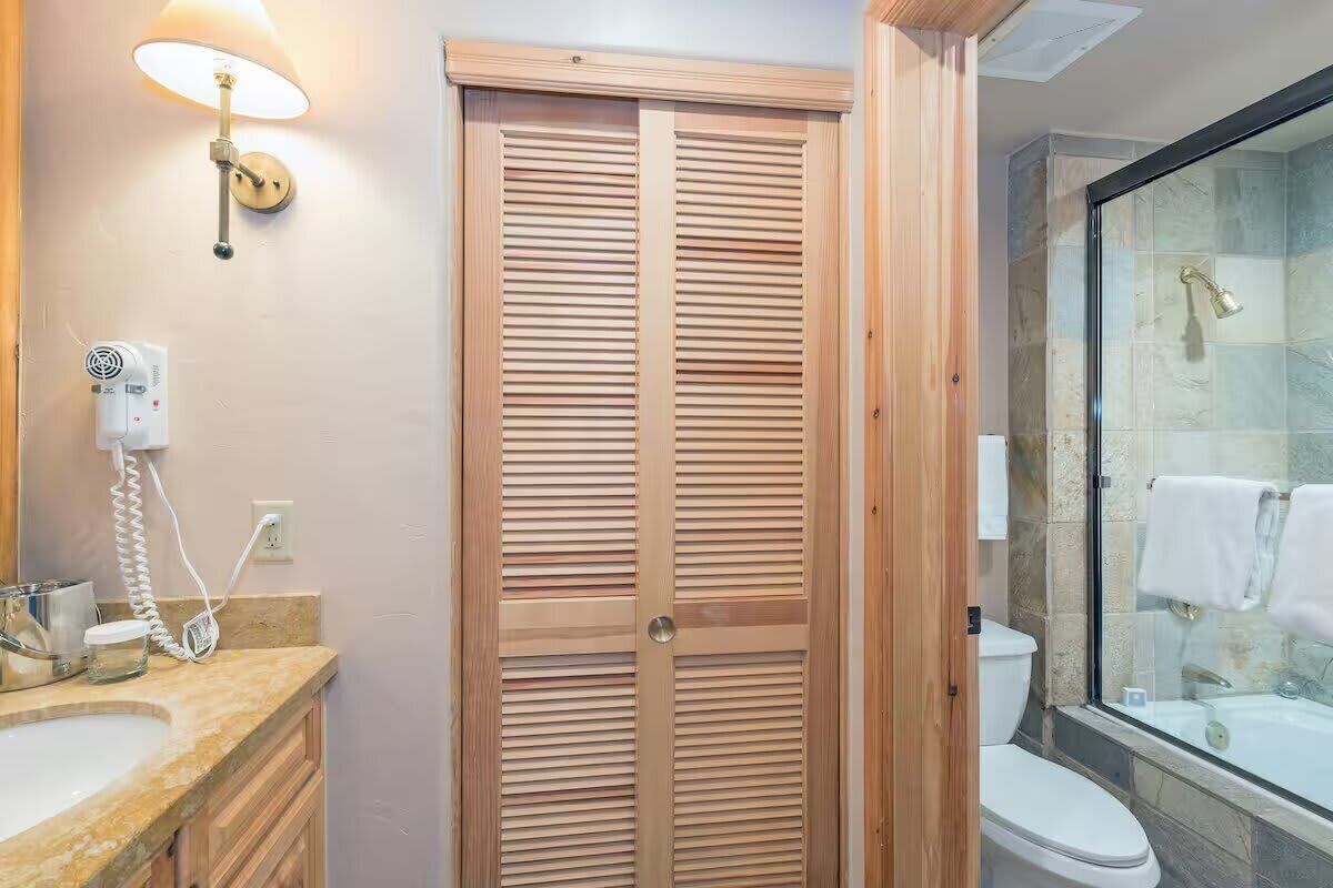 A bathroom with a wooden door, a shower with a glass enclosure, a toilet, and a sink with a mirror.