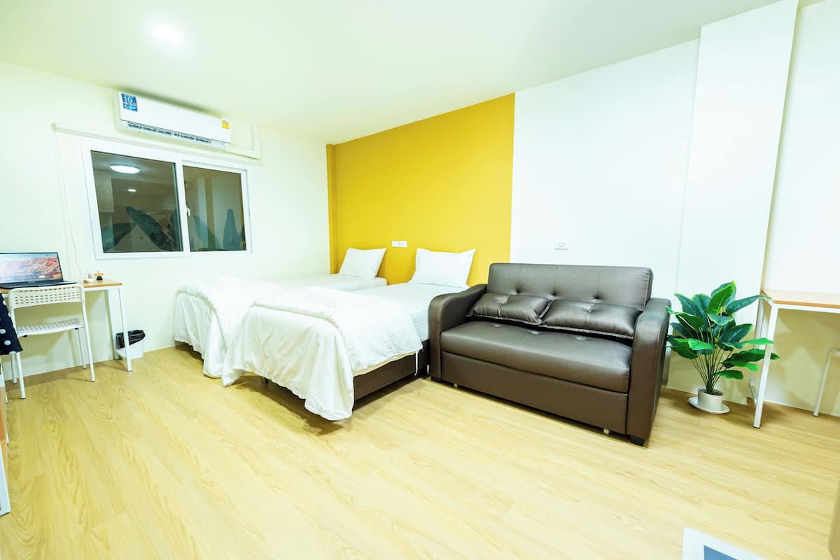 A room with a bed, a brown leather sofa, a small table, and a potted plant.
