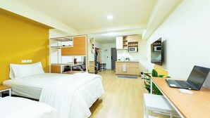 A hotel room with two beds, a desk with a laptop, a microwave, and a small kitchenette.