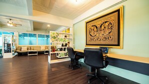 A modern office space with a wooden floor, a sofa, two office chairs, a desk with a computer, and a large framed artwork on the wall.