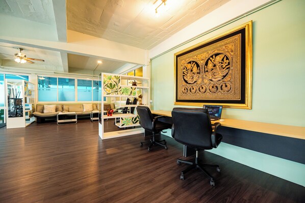 A modern office space with a wooden floor, a sofa, two office chairs, a desk with a computer, and a large framed artwork on the wall.
