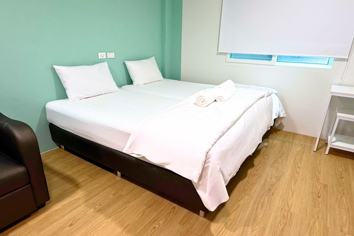 A single bed with white bedding in a room with light green walls and wooden flooring.