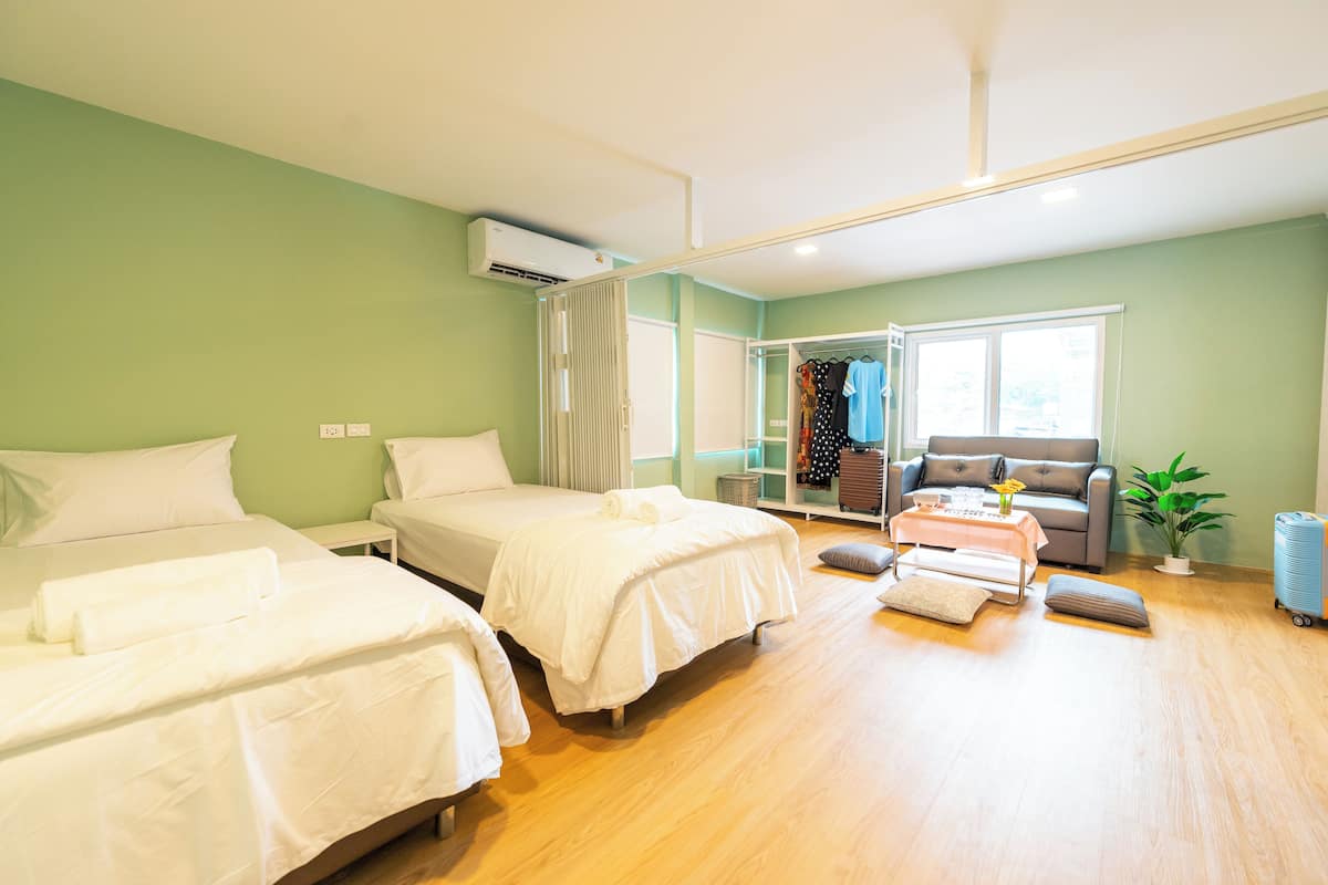 A hotel room with two beds, a sofa, a small table with a vase, and a window.