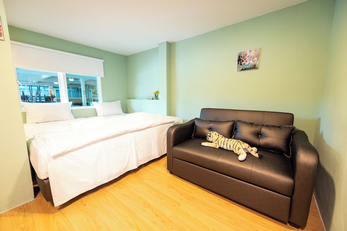 A bedroom with a bed, a brown leather sofa, a window, and a wall-mounted picture.