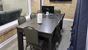 A conference room with a long table, chairs, a flat-screen TV, and a window with a view of outdoor furniture.