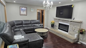 A living room with a black leather sofa, a round coffee table, a fireplace, and a mounted TV.
