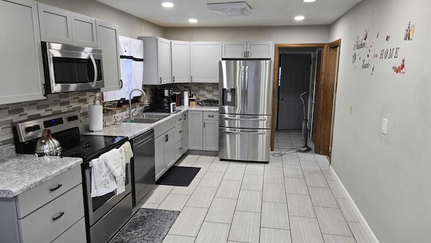 A modern kitchen with stainless steel appliances, grey cabinets, and a tiled floor.