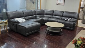 A modern living room with a dark wood floor, a black leather sectional sofa, a round coffee table, and a chandelier.