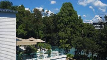 A residential area with a white building, a balcony with a green railing, and a large tree in the background.