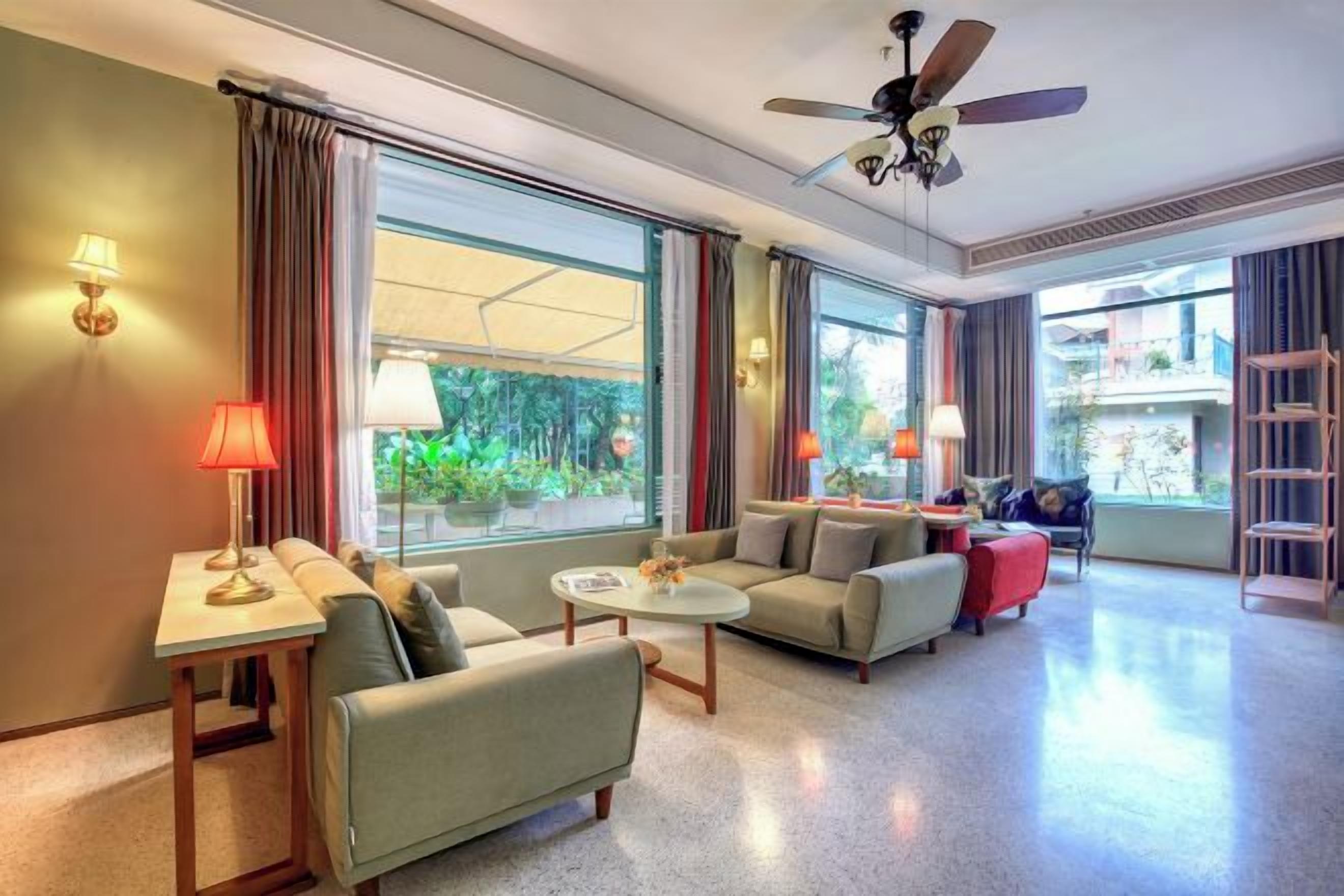 A hotel room with a sofa, armchair, table, and a ceiling fan.