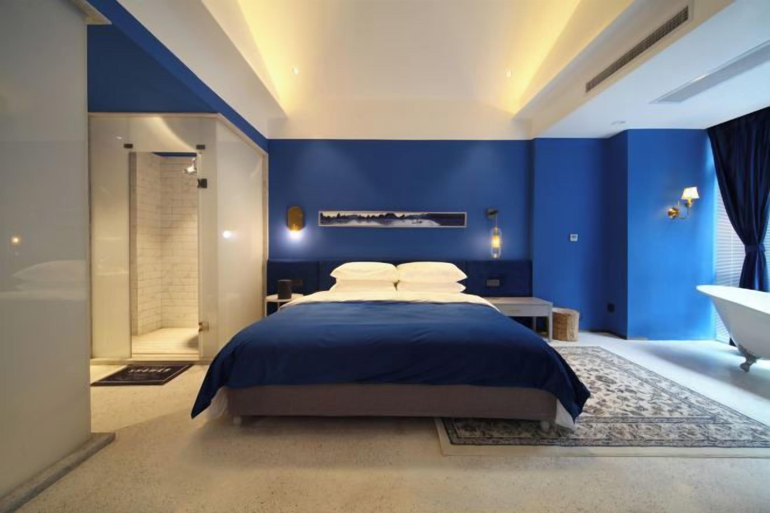 Een moderne slaapkamer met een groot bed, een inloopkast, een badkuip en een wandlamp.