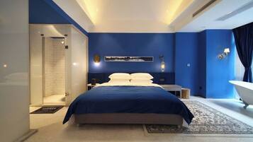 Een moderne slaapkamer met een groot bed, een inloopkast, een badkuip en een wandlamp.
