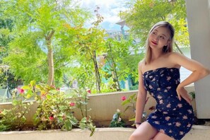 A person in a strapless dress with a floral pattern, standing in an outdoor area with greenery and a building in the background. - Julan'an Homestay (Guilin Liangjiang Sihu Dongxi Alley Shop) (Guilin)