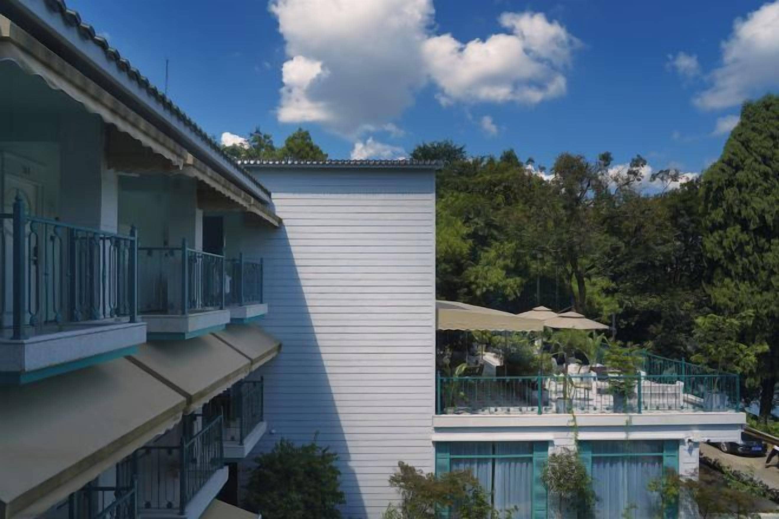 A multi-story building with balconies, a pool area, and a view of a forested hillside.